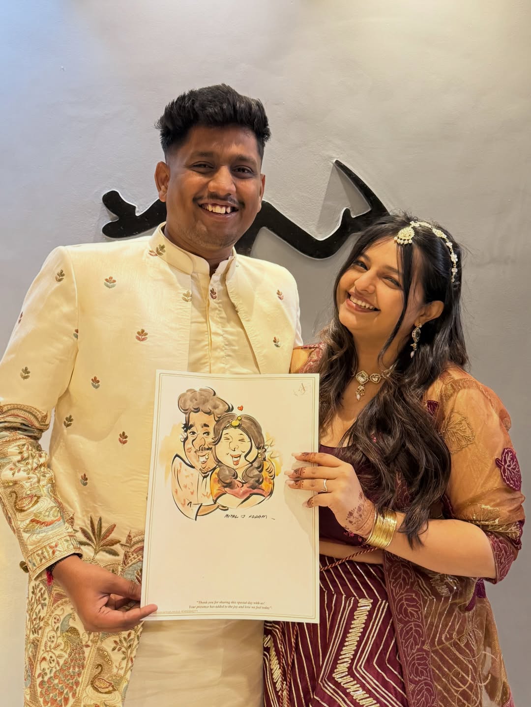 Live wedding caricature artist sketch held by Indian couple in cream sherwani and maroon lehenga