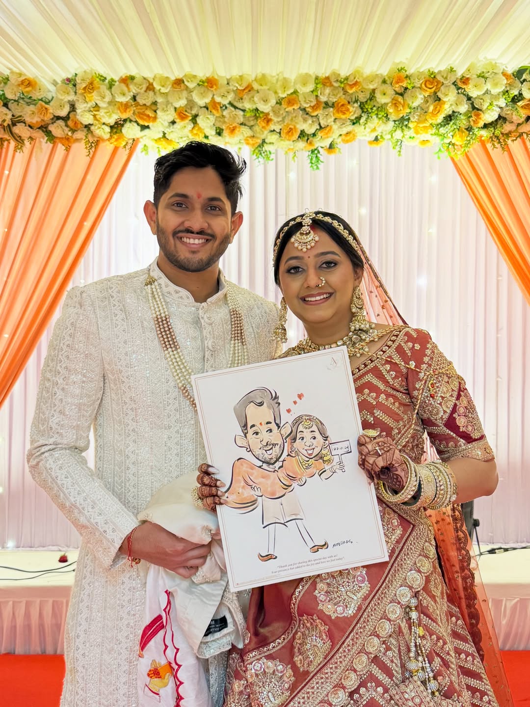 Bride and groom holding a hand-drawn live wedding caricature under a floral mandap