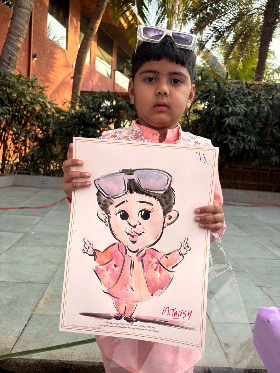 Little boy Mitansh holding his own live kids caricature in pink kurta with sunglasses
